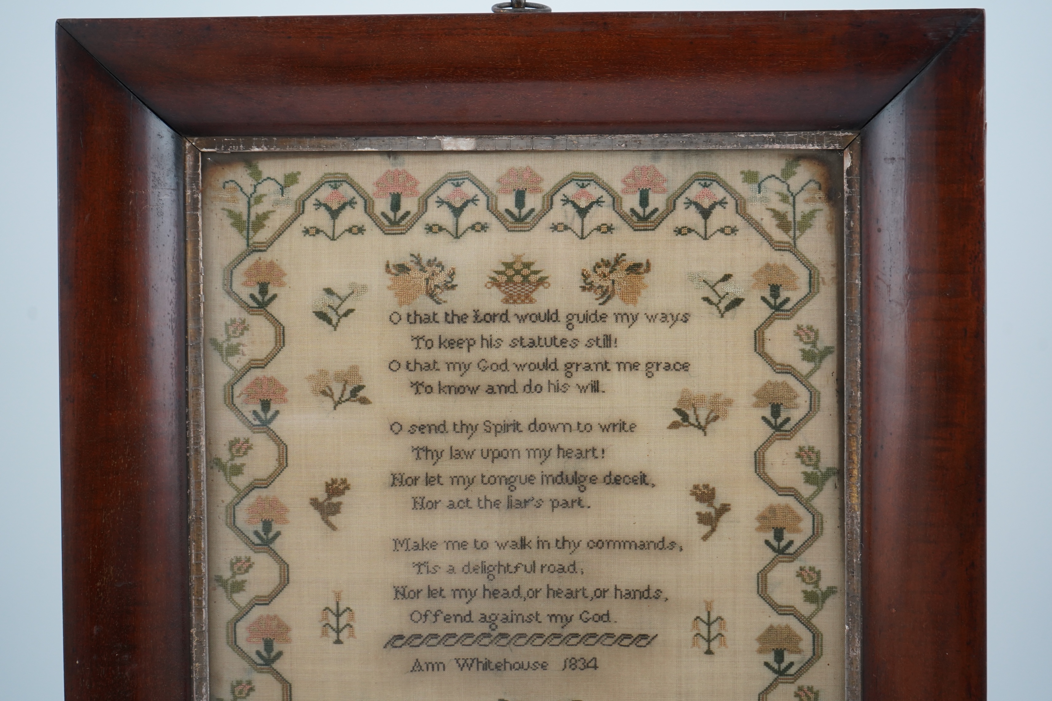 A wide mahogany framed sampler by Ann Whitehouse dated 1834, worked in coloured silks on a fine linen ground, in small stitches, bordered with a geometric stylistic vining pattern, set with a central verse, above her nam